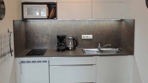 Una cocina compacta equipada con microondas, cafetera y lavabo.
