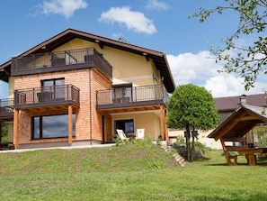 Una casa de dos pisos con un balcón, un pequeño jardín y una mesa de picnic.