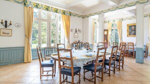 Une salle à manger avec une grande table dressée pour six personnes, entourée de chaises en bois dotées de coussins bleus.