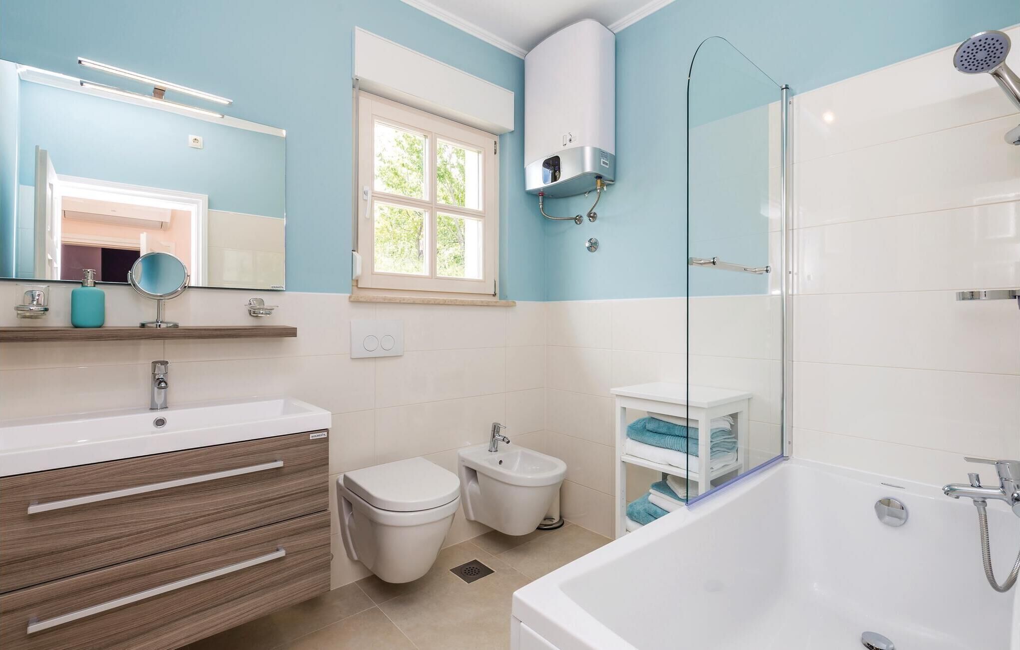 A modern bathroom with a bathtub, toilet, bidet, and a large mirror.
