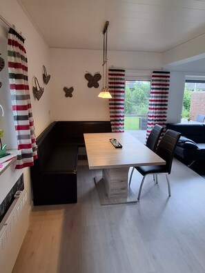 A modern living room with a wooden dining table, black sofa, and striped curtains. - Vacation cottage Sander, Germany (Friedrichskoog)