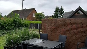An outdoor patio with a table and chairs, surrounded by a brick wall and greenery. - Vacation cottage Sander, Germany (Friedrichskoog)