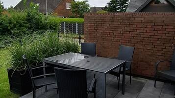 Patio esterno con tavolo e sedie, circondato da un muro in mattoni e piante.