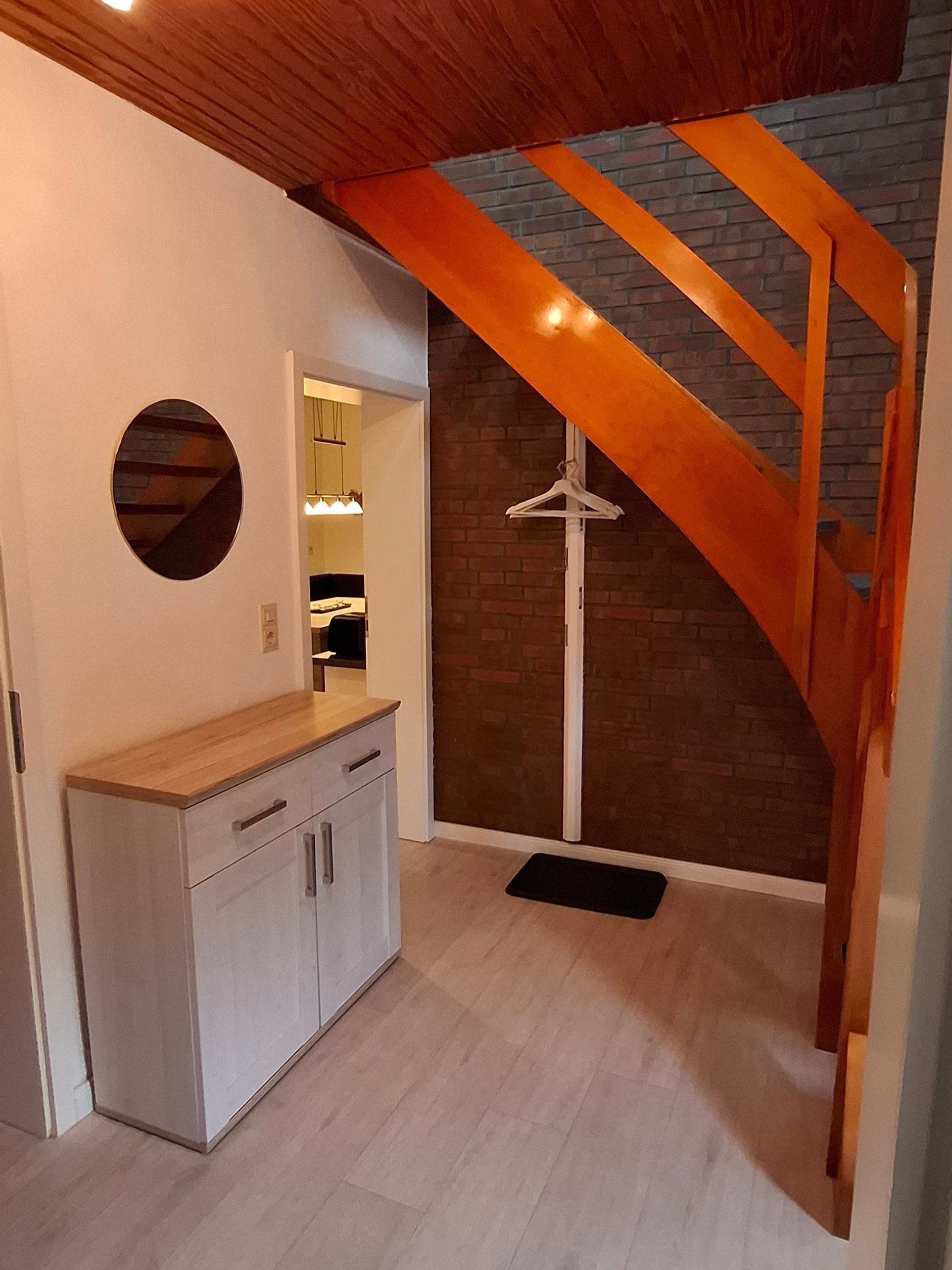 A compact room with a wooden ceiling, a white cabinet, a hanging clothes rack, and a brick wall.