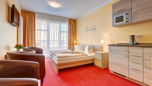 Quarto de hotel com cama, escrivaninha, cadeira, micro-ondas e cozinha compacta.