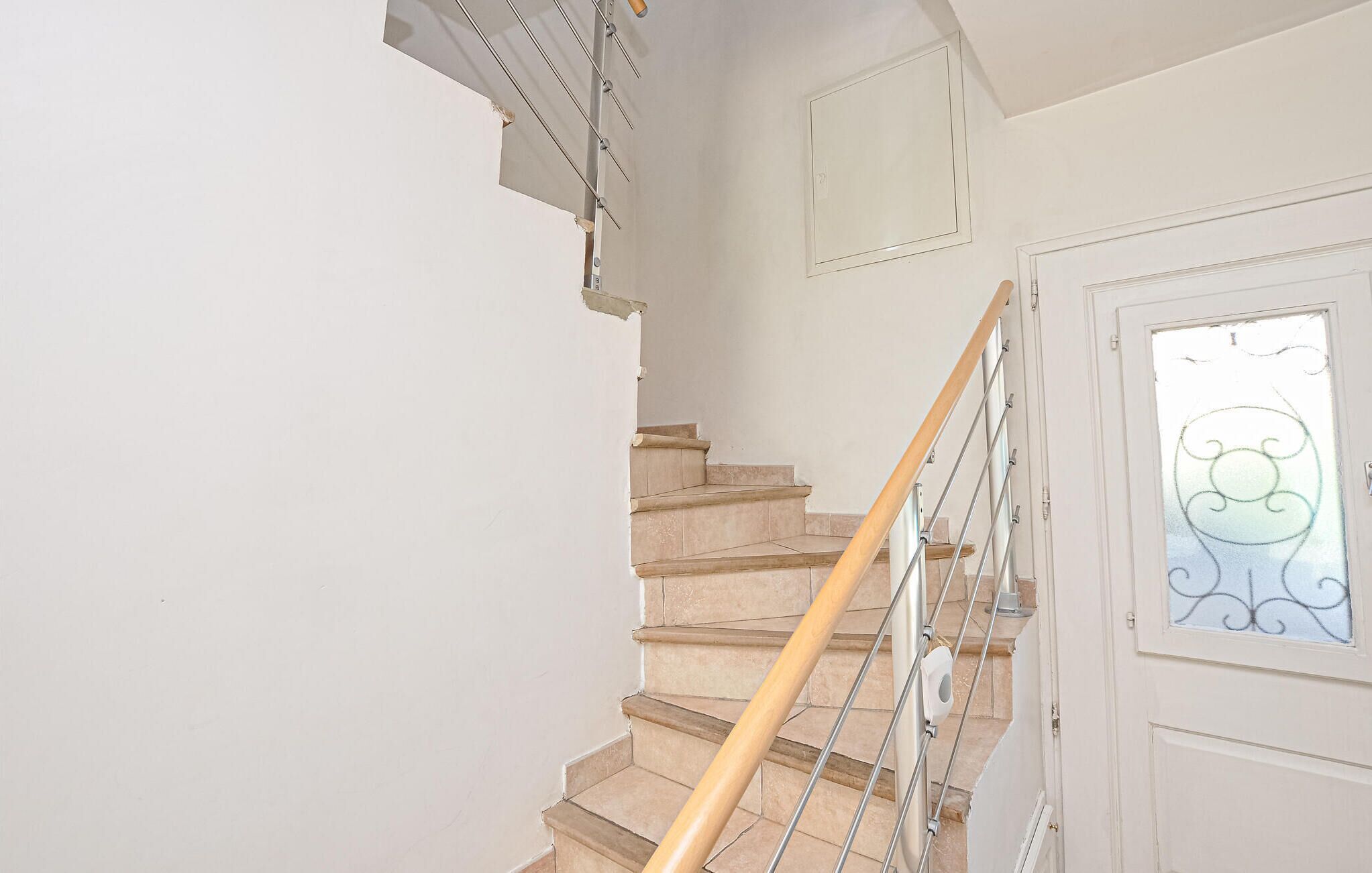 A staircase with a wooden handrail and metal balusters, leading to a door with a frosted glass panel.