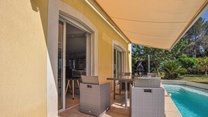 Ein überdachter Patio-Bereich mit Gartenmöbeln, einem Pool und einem Grill.