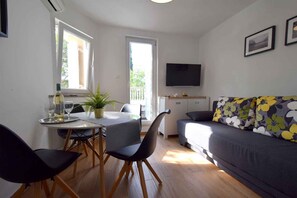 Un espace de vie compact comprenant un coin repas, un canapé, un téléviseur à écran plat et un balcon.