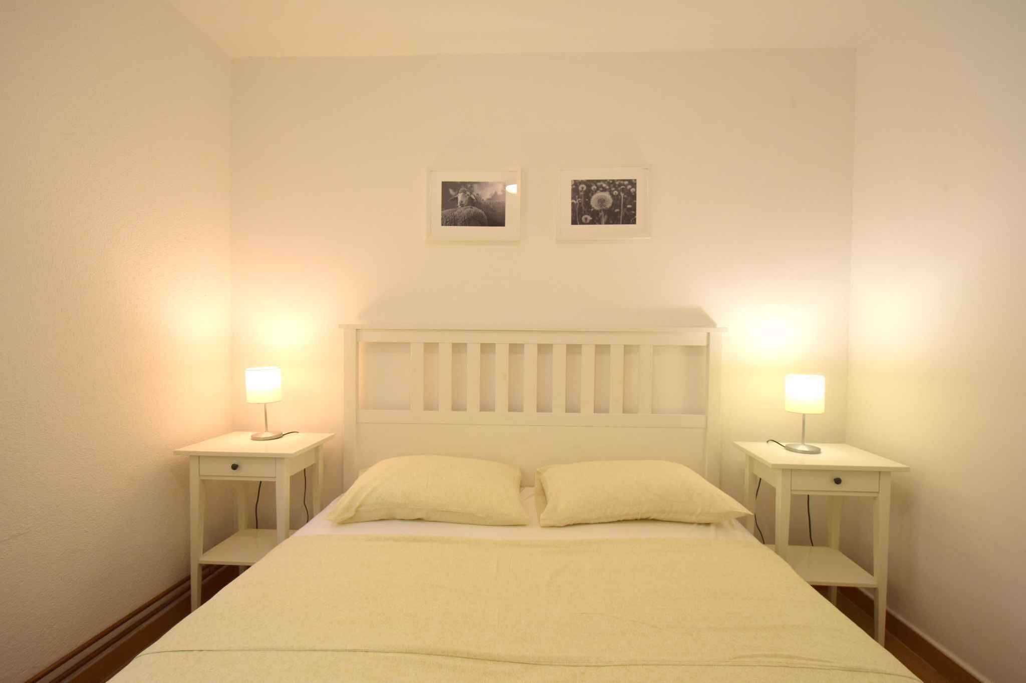 Ein Zimmer mit einem Einzelbett, einem weißen Kopfteil, zwei Nachttischen mit Lampen und zwei gerahmten Bildern an der Wand.