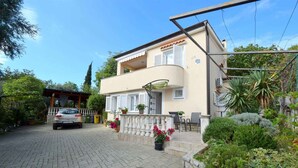 A two-story house with a balcony, a car parked in front, and a garden with various plants. - Holiday apartment mit Klimaanlage und Meerblick (Čižići)