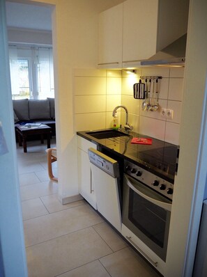 A compact kitchen with a dishwasher, stove, and a hanging rack for utensils.