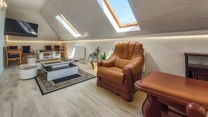 Ein geräumiges Loft mit hohen Decken, Dachfenstern, einem großen Flachbildfernseher und einer gemütlichen Sitzecke mit Ledersessel und Hocker.