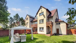 Ein zweistöckiges Haus mit überdachter Terrasse, Rasen und Holzzaun.
