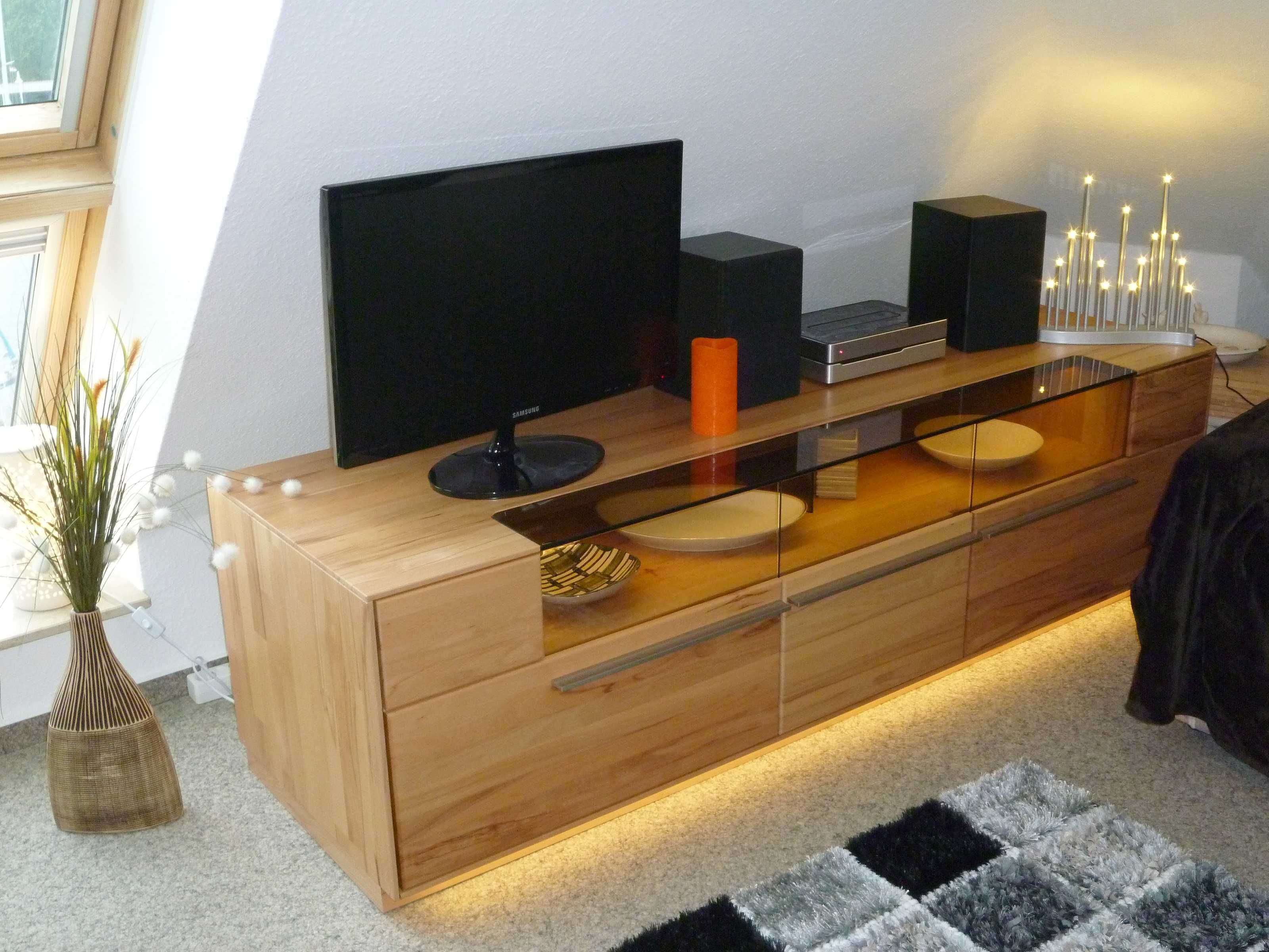 Ein modernes Wohnzimmer mit einem Holzkasten, einem Flachbildfernseher, einem Glastisch und einem dekorativen Kerzenhalter.