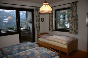 A bedroom with two beds, a window with curtains, a wooden headboard, and a hanging light fixture. - Haus Konradgut - apartment number 13 (St. Lorenzen ob Murau)