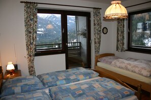 A bedroom with two beds, a window with a mountain view, a balcony, and a lamp.