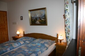 Ein Schlafzimmer mit einem hölzernen Bett, zwei Nachttischlampen, einem Bild an der Wand und einem blumigen Vorhang.