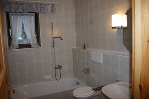 Ein Badezimmer mit Badewanne, Toilette und einem fensterbehangenen Fenster.