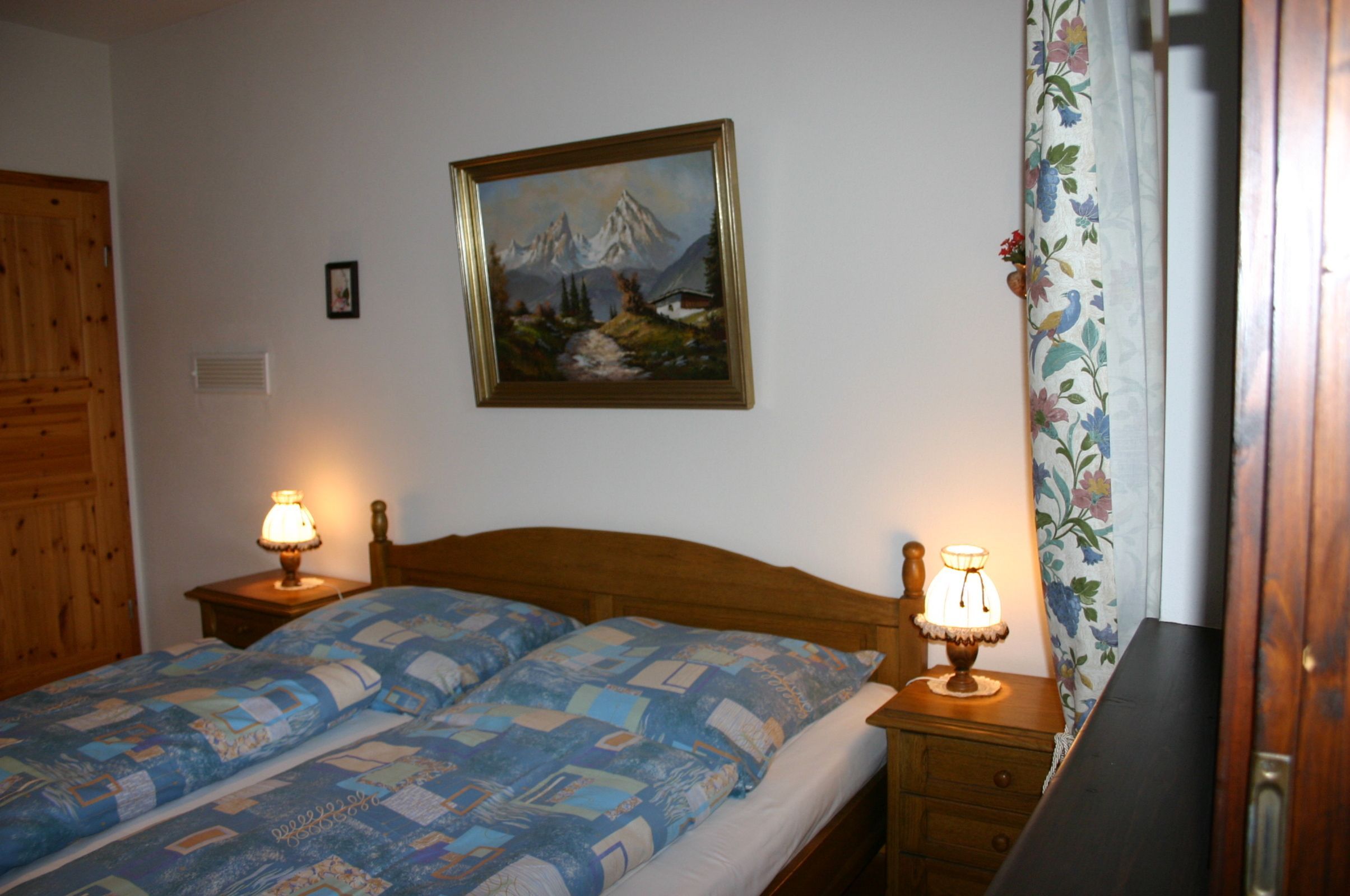 Une chambre à coucher avec un lit en bois, deux lampes de chevet, un tableau au mur et un rideau à motifs floraux.