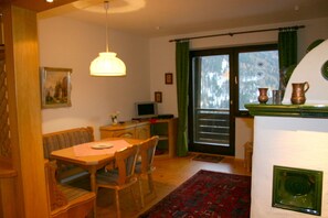 A dining area with a wooden table, chairs, a hanging light fixture, a television, and a window with curtains.