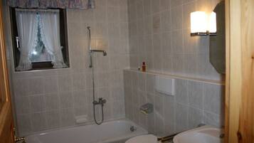 Une salle de bain avec une baignoire, des toilettes et une fenêtre avec des rideaux.