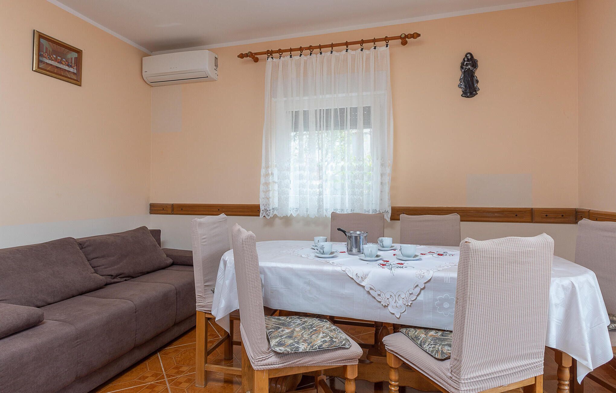 Ein Essbereich mit einem Tisch für vier Personen, einem braunen Sofa und einem Fenster mit Spitzenvorhängen.