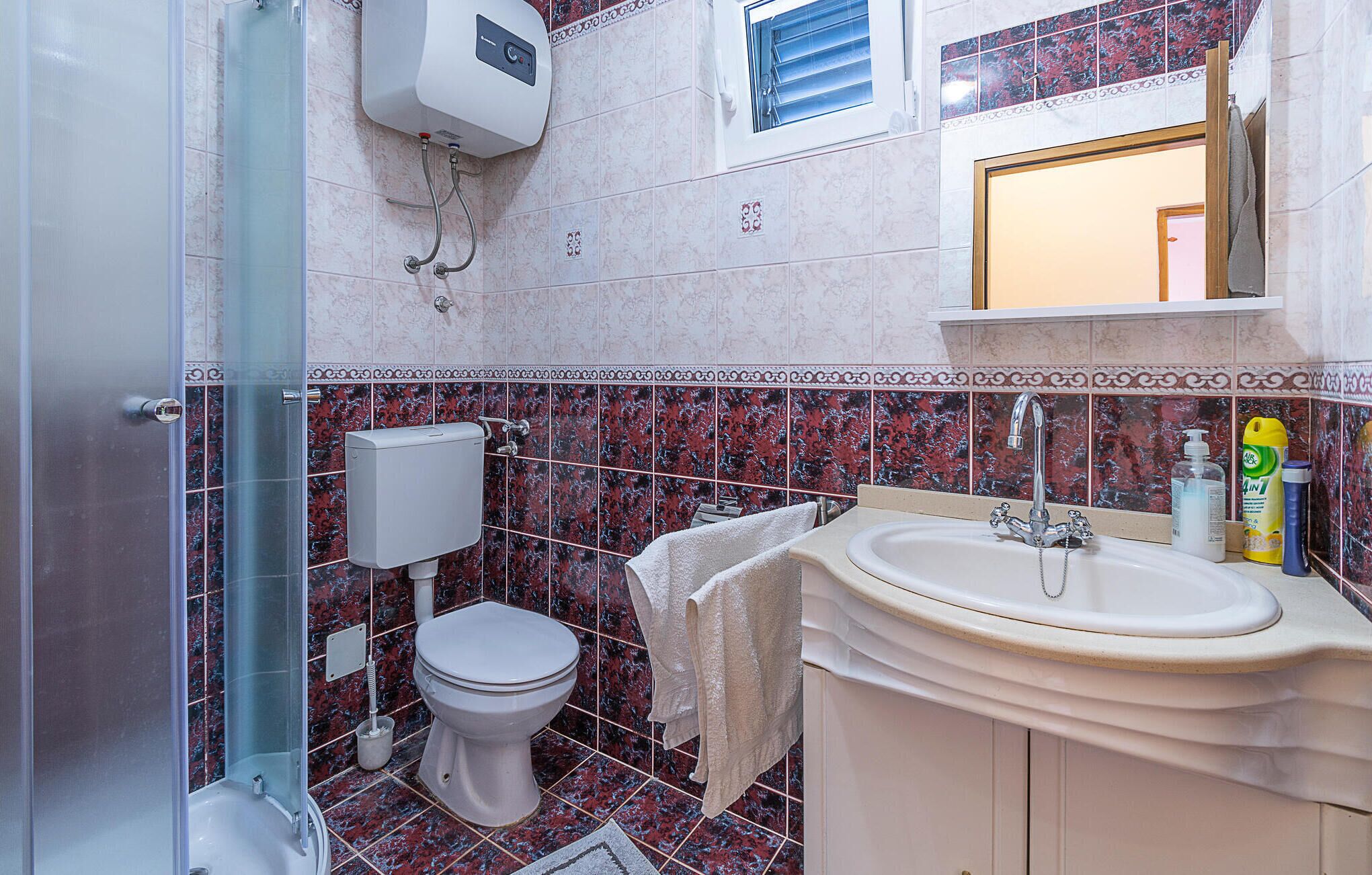 A bathroom with a shower, toilet, sink, and a window above the mirror.
