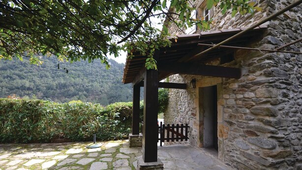 Edificio de piedra con una pérgola de madera y un camino de piedra que lleva a una puerta.