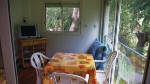 A dining area with a table covered in a floral tablecloth, white chairs, and a television on a wooden stand. - Nice apartment in Sagone with kitchen (Sagone)