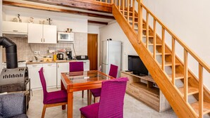 Uma cozinha compacta com eletrodomésticos modernos, uma área de jantar com mesa de vidro, cadeiras roxas e uma escada de madeira.