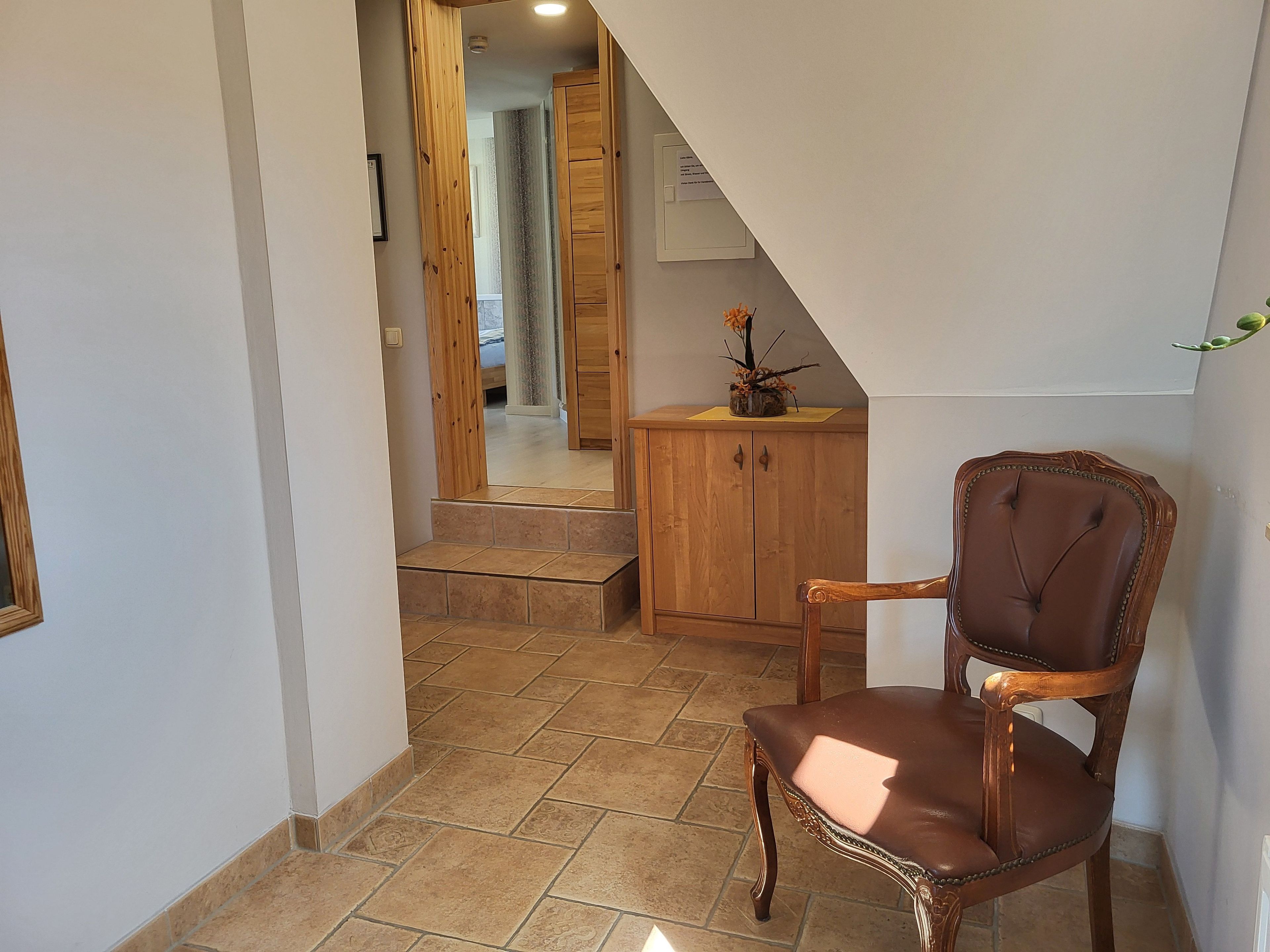 A hallway with a wooden chair, a cabinet, and a staircase leading to another room.