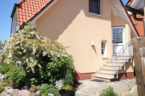 A building with a red-tiled roof, beige walls, a small window, and a staircase leading to the entrance.