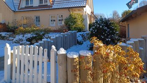 Une maison avec un toit en tuiles, une clôture blanche et un sol recouvert de neige.