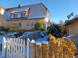 Une maison avec un toit en tuiles, une clôture blanche et un sol recouvert de neige.
