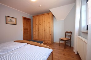 A bedroom with a bed, a wooden wardrobe, a chair, and a radiator.