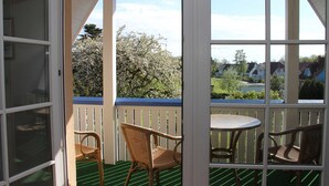 Un espace extérieur abrité, équipé d’une table et de deux chaises, offrant une vue sur un quartier résidentiel et délimité par une clôture en bois.
