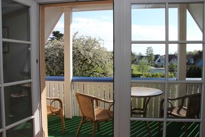 Un espace extérieur abrité, équipé d’une table et de deux chaises, offrant une vue sur un quartier résidentiel et délimité par une clôture en bois.