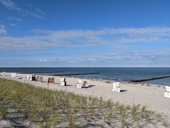 A beach with white lounge chairs and a wooden structure labeled with numbers.