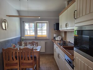 Een keuken met houten kasten, een raam, een eettafel met stoelen en een magnetron.