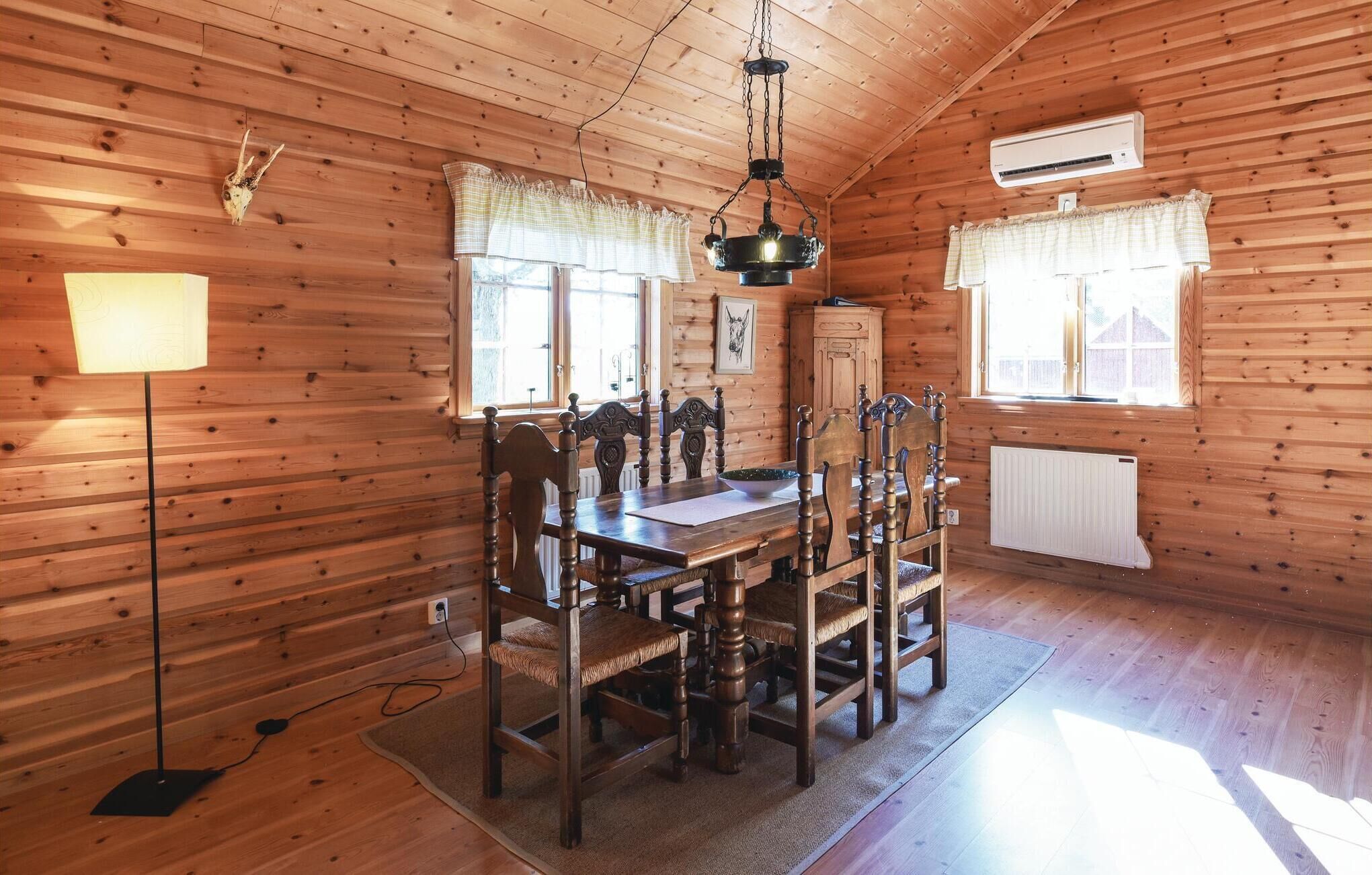 A wooden cabin interior with a dining table, chairs, a chandelier, and a radiator.