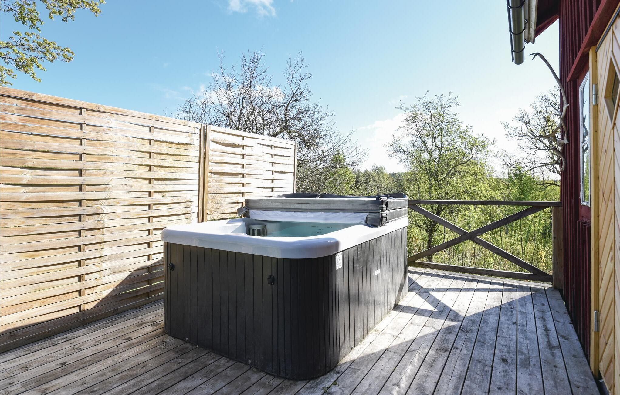 Un bain à remous sur une terrasse en bois, avec une clôture en bois et des arbres en arrière-plan.