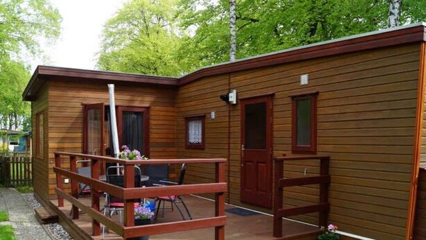 A wooden cabin with a deck, a small porch, and a single door.