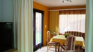 A dining area with a table set for two, a television on a stand, and a window with curtains.