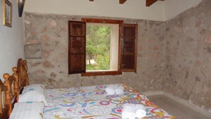 A bedroom with a bed, wooden headboard, a window with open shutters, and a view of greenery outside.
