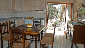 A kitchen with a dining area, wooden chairs, a table with fruit, and a view through a door.