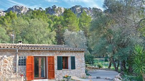 A stone building with a tiled roof, wooden shutters, and a gravel driveway.