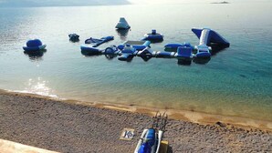 Una playa con agua cristalina, orilla de guijarros y varios objetos azules flotando.