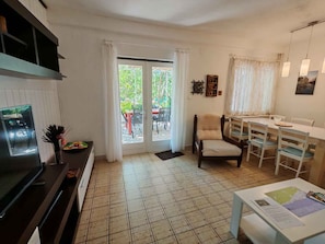 Uma sala de estar com televisão, mesa de jantar, cadeiras, sofá e porta de vidro deslizante para área externa.