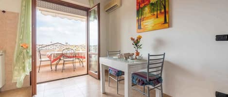 A dining area with a table and chairs, a painting on the wall, and a view through a glass door.