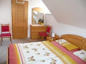 A bedroom with a bed, a dresser, two chairs, a mirror, and a lamp. - Apartment OG - Apartment / DZ Blesse Allstedt (Allstedt)